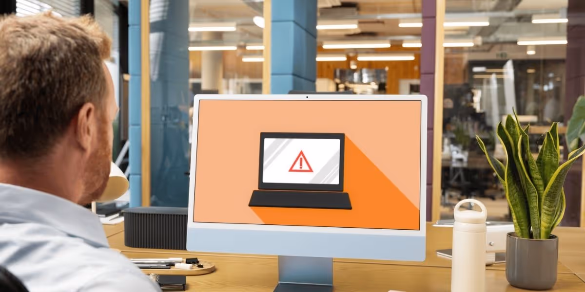 Man in office looking at a computer screen displaying a warning symbol, indicating a possible security or system alert.