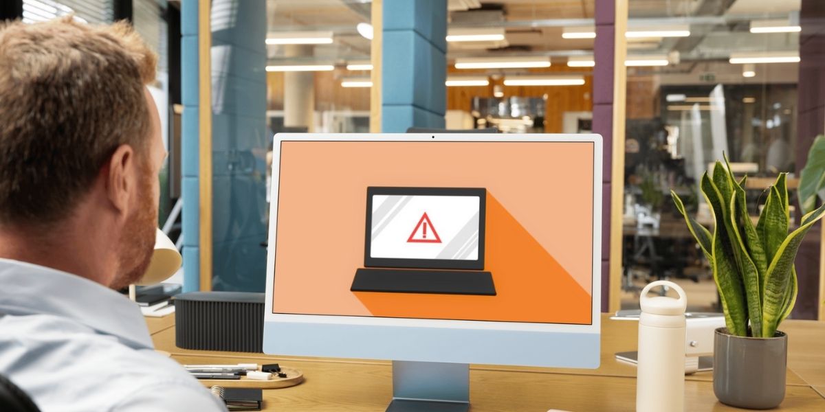 Man in office looking at a computer screen displaying a warning symbol, indicating a possible security or system alert.