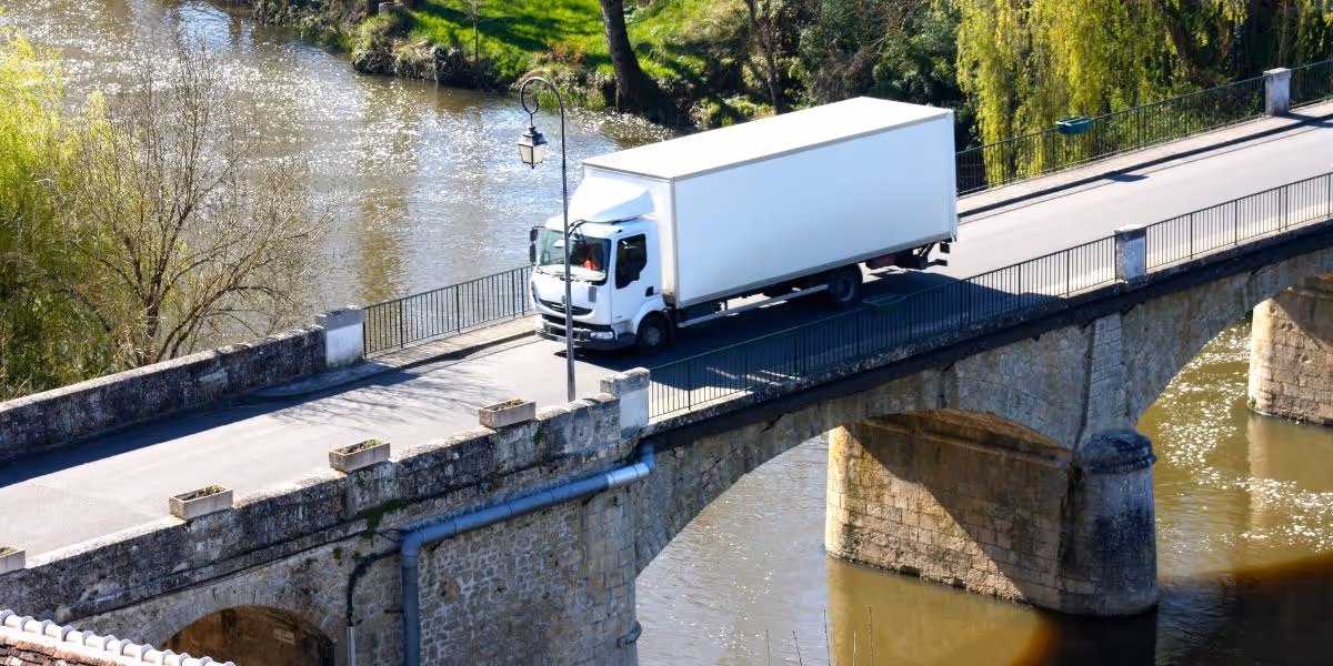 Two delivery workers unloading cardboard boxes from the back of a white van outside a warehouse, with several large parcels stacked on the ground nearby