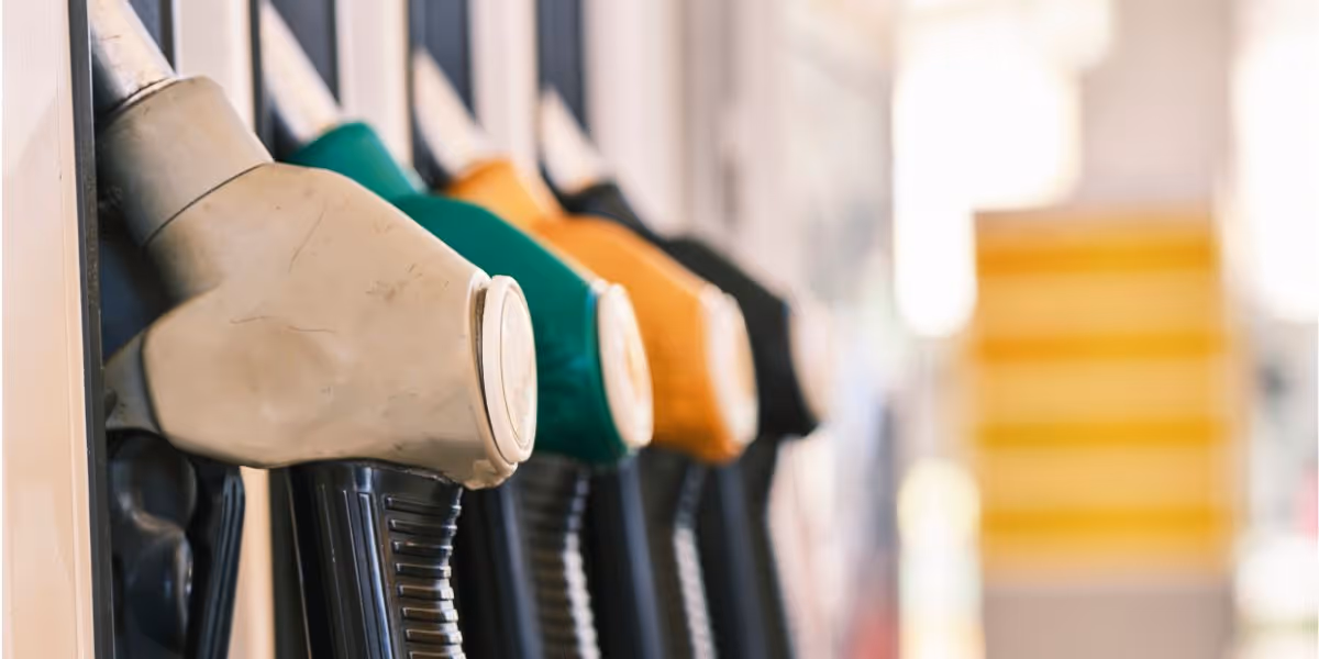 Close-up view of four fuel pump nozzles at a petrol station, coloured grey, green, yellow, and black arranged side by side in their holders.