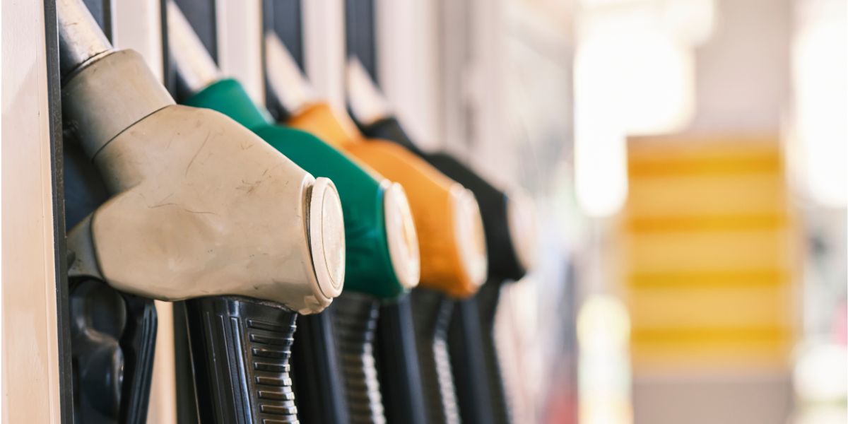 Close-up view of four fuel pump nozzles at a petrol station, coloured grey, green, yellow, and black arranged side by side in their holders.