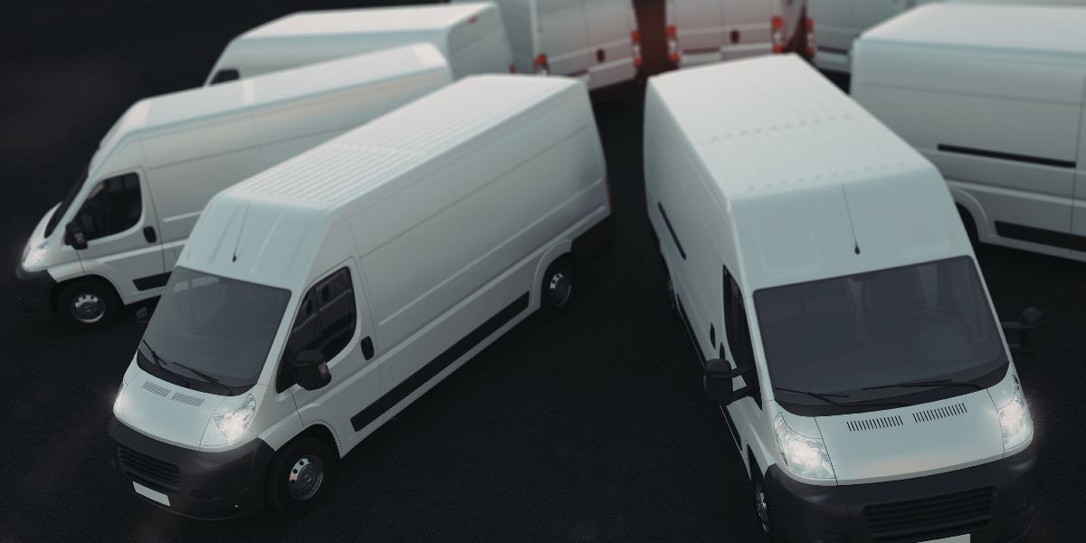 White delivery vans parked closely together in a dark lot, viewed from above, forming a tight cluster of similar vehicles.