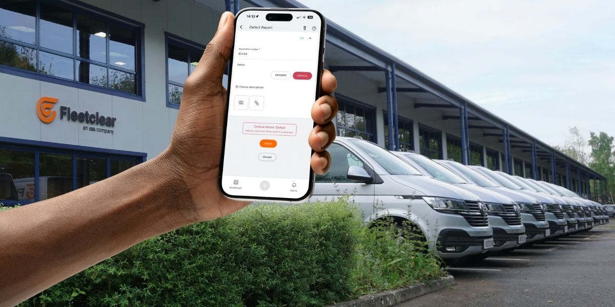 A hand holds a smartphone in front of a Fleetclear building and a row of white vans. The phone screen shows a defect reporting app, suggesting fleet maintenance or inspection management.