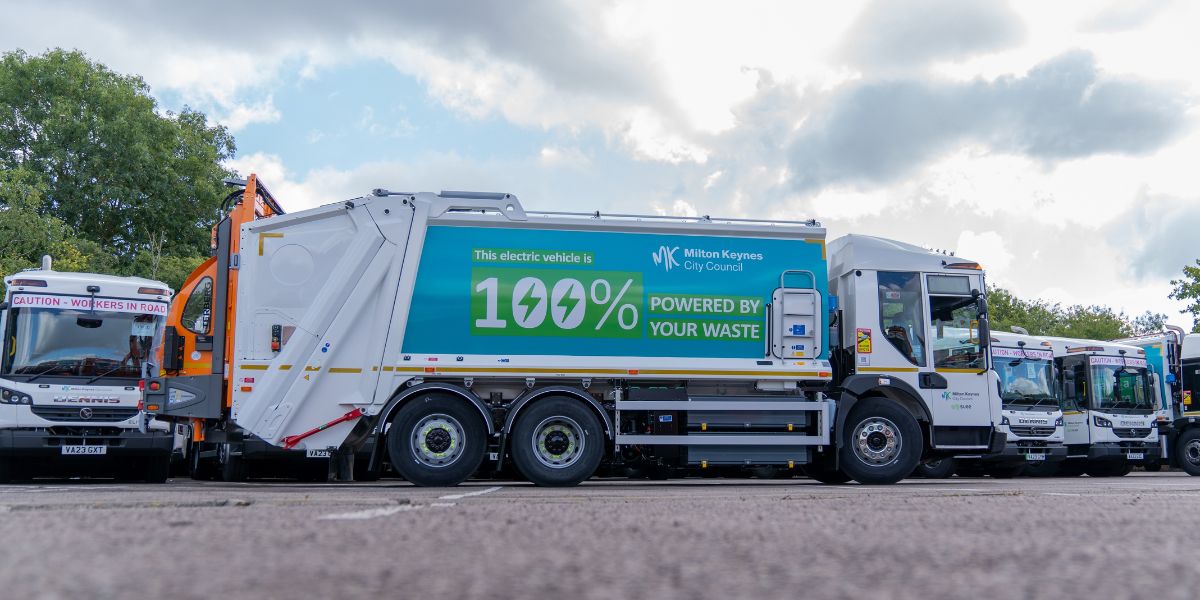 Electric refuse collection vehicle operated by Milton Keynes City Council and SUEZ, branded “100% powered by your waste,” parked with other fleet vehicles, showcasing a modern, low-emission waste collection fleet.