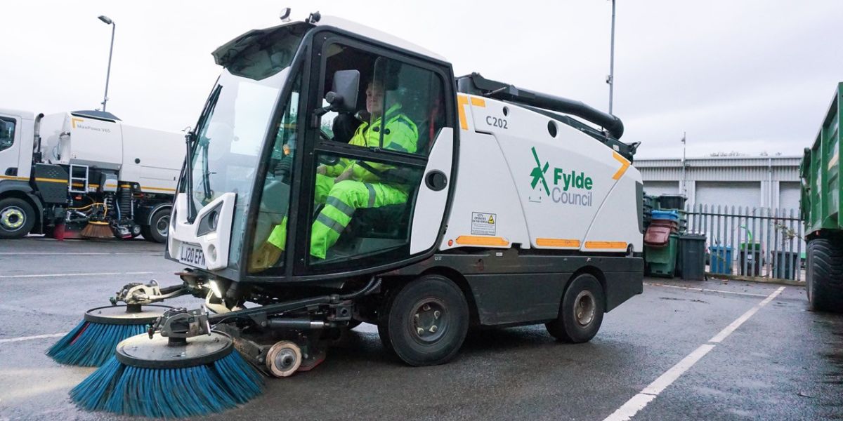 Fylde Council road sweeper parked in a depot yard, with an operator in high-visibility clothing seated inside the cab.