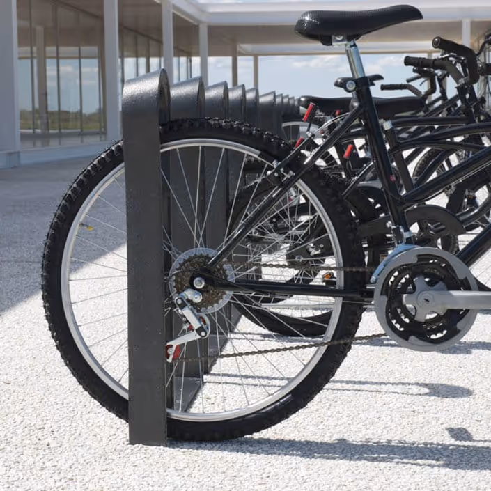 Fila de bicicletas negras estacionadas aseguradas en un soporte metálico en un espacio exterior con piso gris.
