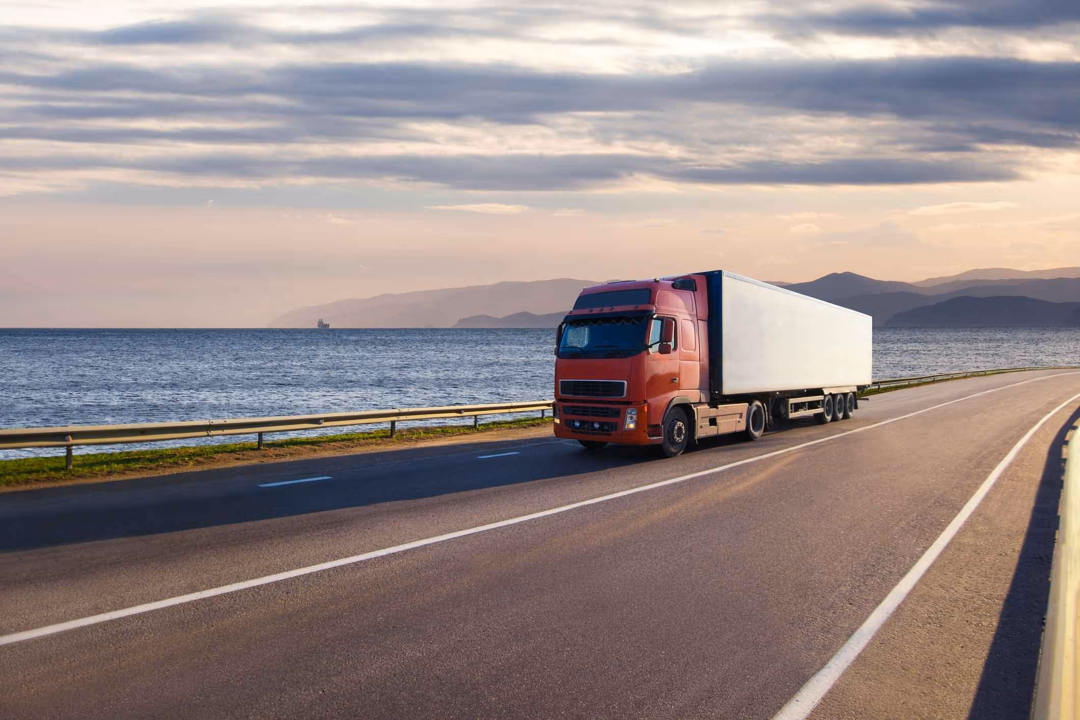 Red semi-truck driving along coastal highway, representing the work of a San Diego truck accident lawyer.