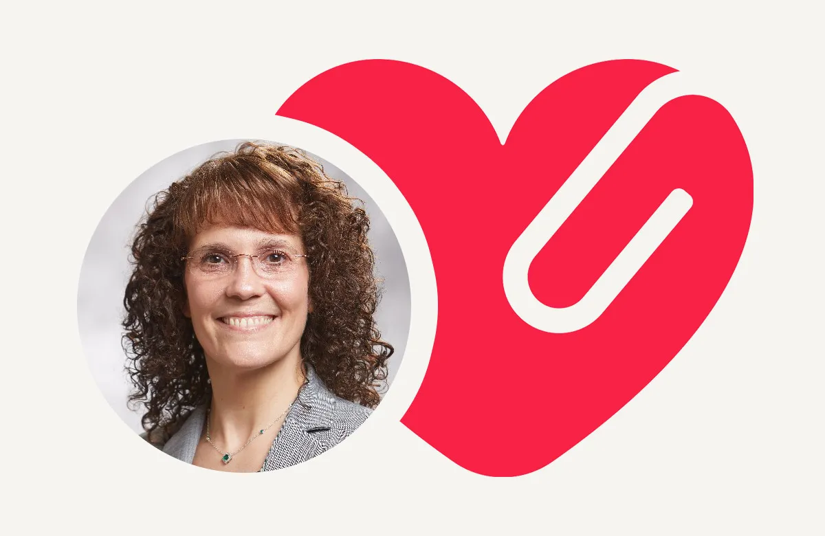 Smiling woman with curly hair and glasses inside a circle beside a large red heart logo.