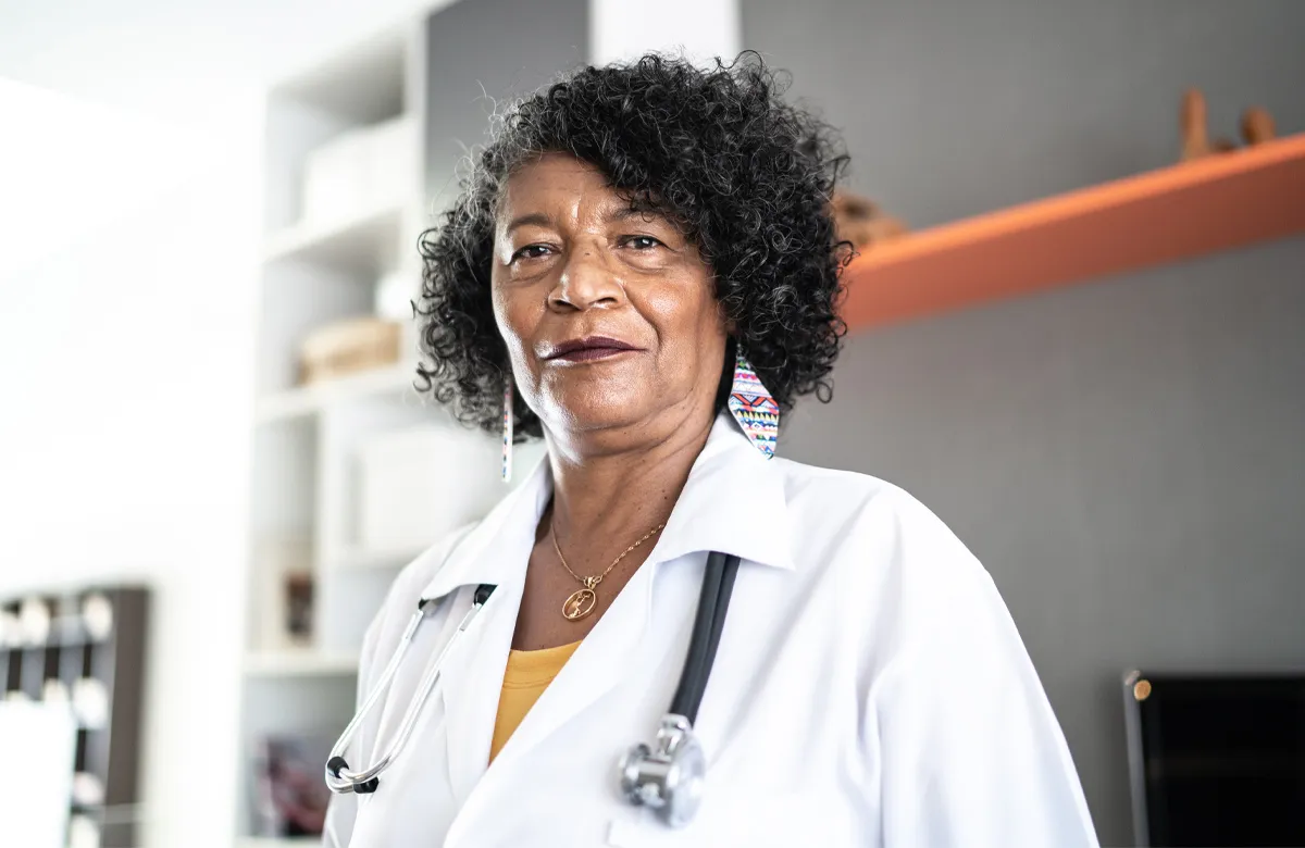 Confident female doctor wearing a white coat and stethoscope in a modern medical office.