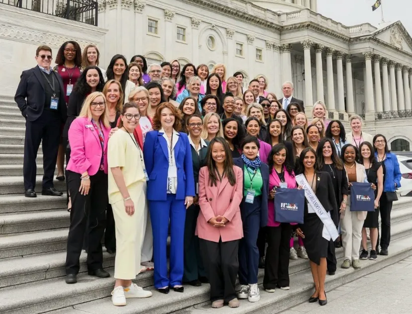 Large diverse group of professional women standing on steps outside a large classical government building.