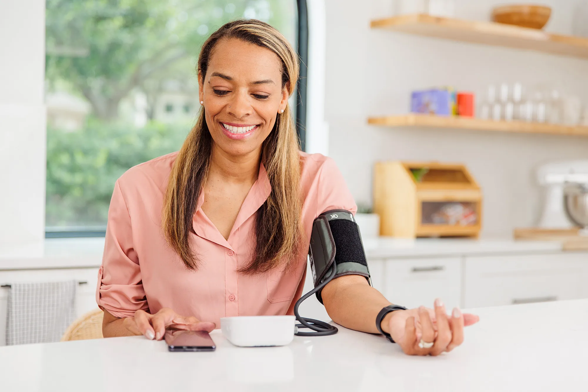 Woman checks her blood pressure using an automated cuff at home while smiling.