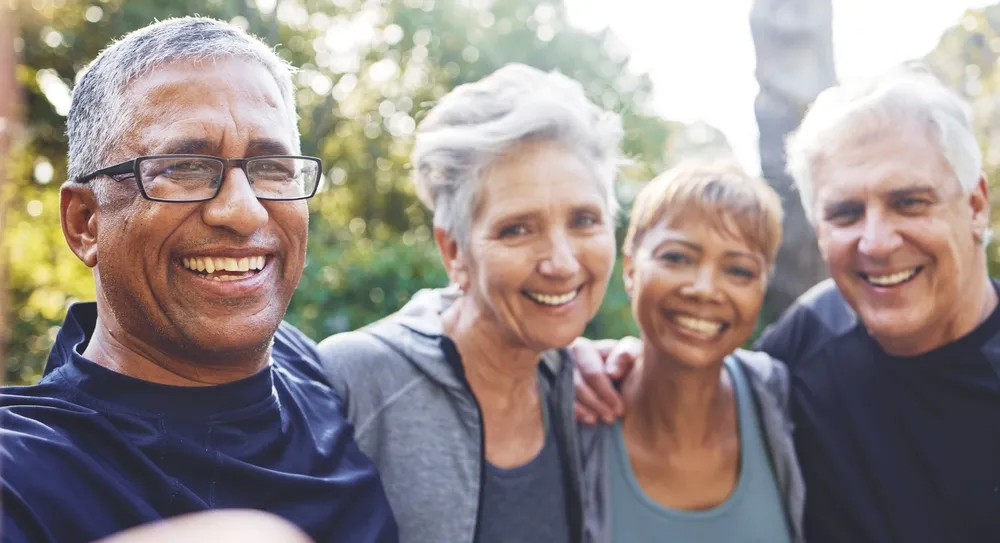 Smiling diverse group of four mature adults posing closely outdoors in casual sportswear.