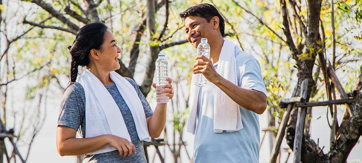 Man and woman outdoors with towels around their necks, smiling and holding water bottles.