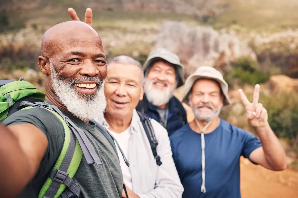 Four older men hiking outdoors smiling, one making peace sign and another giving bunny ears.