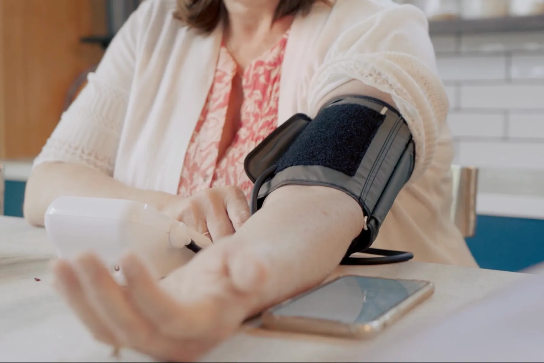 Person using a home blood pressure monitor with cuff on arm and digital display on table.