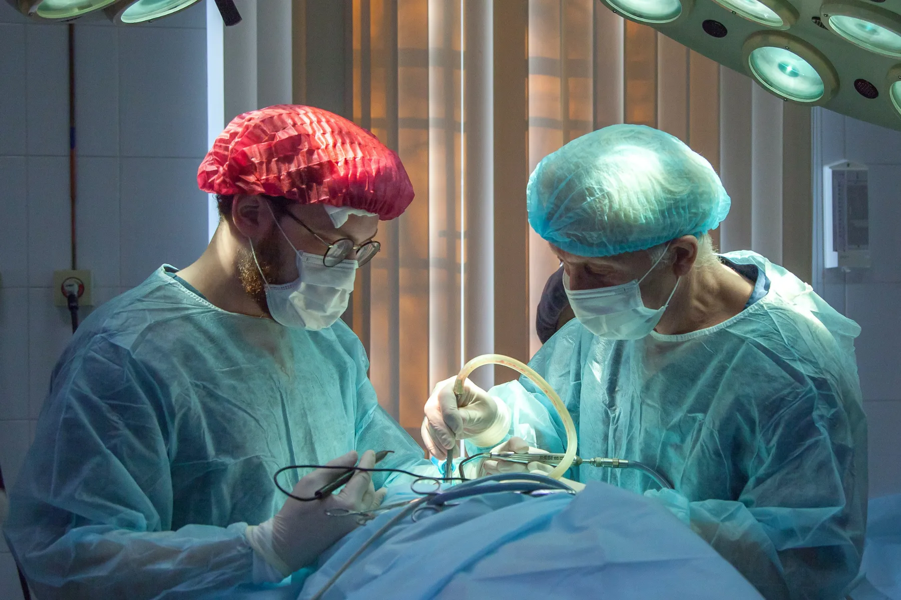 Two surgeons in protective gear performing surgery under operating room lights.