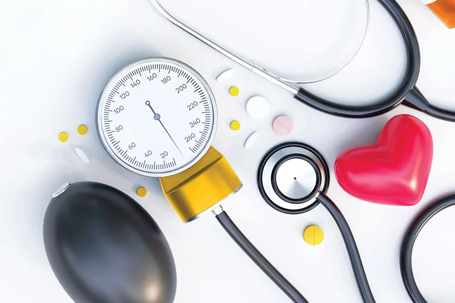 Blood pressure monitor, stethoscope, pills, and red heart model on a white surface.