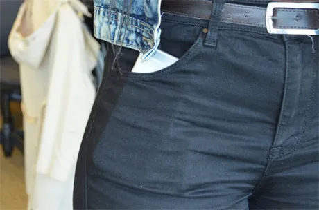Close-up of person wearing black pants with white phone partially visible in front pocket.