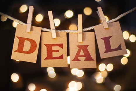 Cards spelling DEAL clipped to a string with clothespins against blurred lights background.