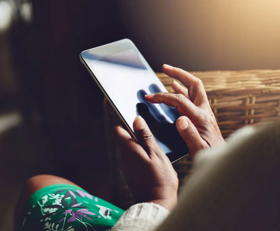 Person using a tablet device with one hand holding and the other tapping the screen indoors.