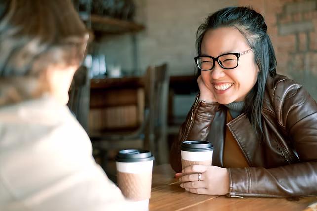Zwei Frauen unterhalten sich lachend bei Kaffee in einem gemütlichen Café.