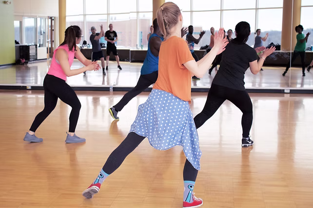 Mehrere Personen tanzen in einem hellen Tanzstudio mit Holzfußboden und Spiegelwand.