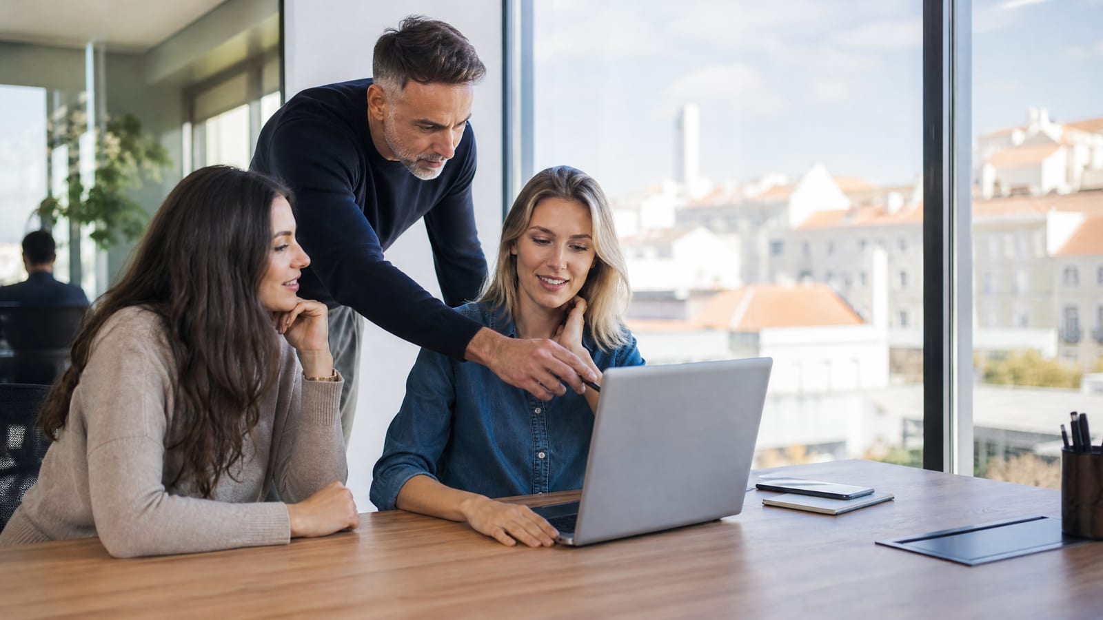 Equipa em escritório analisa um software de CRM no portátil, com um homem a apontar para o ecrã