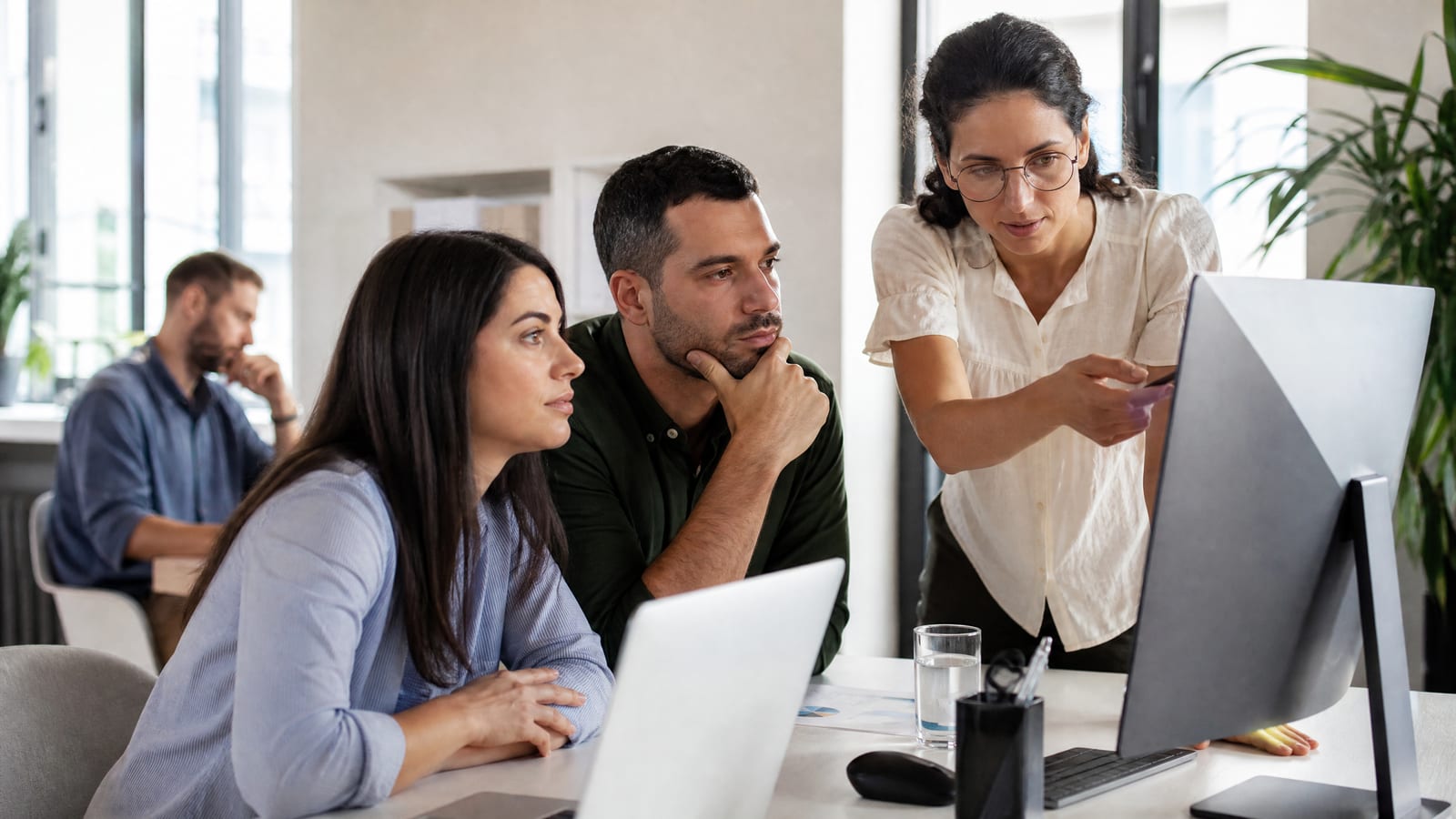 Três colegas num escritório analisam dados no ecrã, enquanto uma mulher aponta para o monitor com google analytics 4