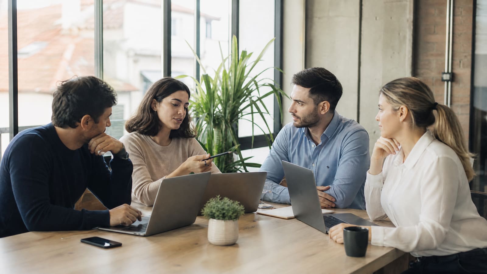 Quatro colegas reunidos à volta de uma mesa com portáteis, a debater software CRM num escritório luminoso