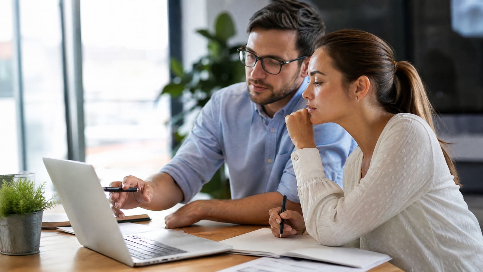 Homem e mulher analisam um portátil num escritório, com notas e canetas, a rever o seo on page do site