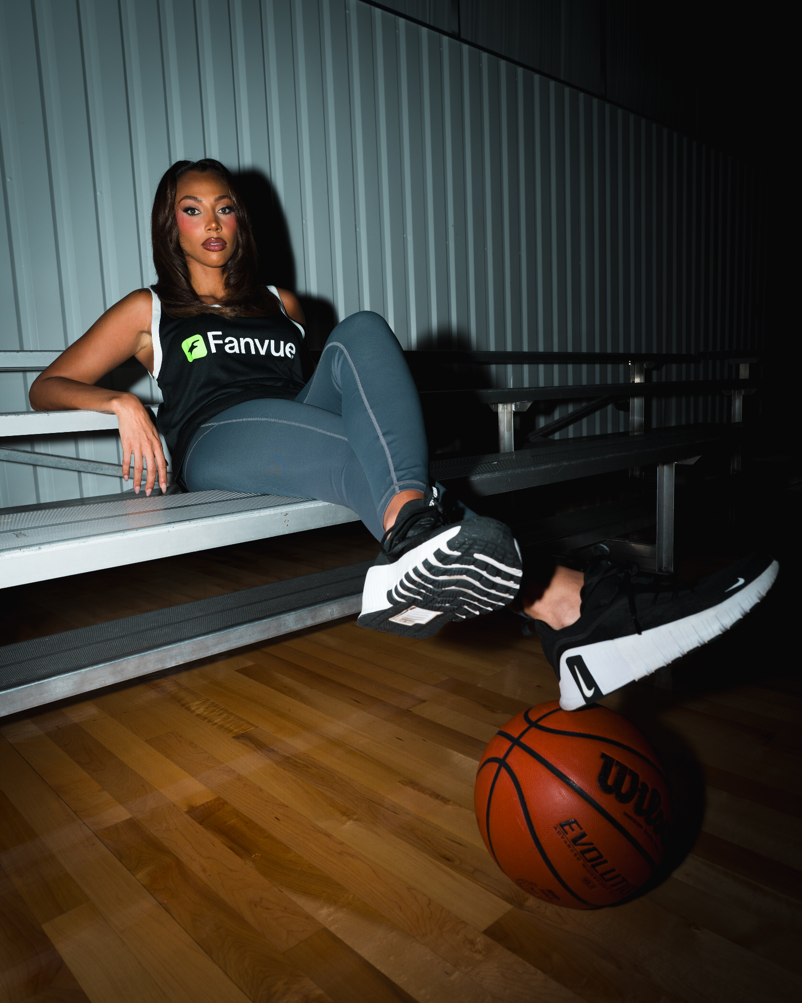 Kysre Gondrezick sitting courtside in a Fanvue jersey with a basketball at her feet.