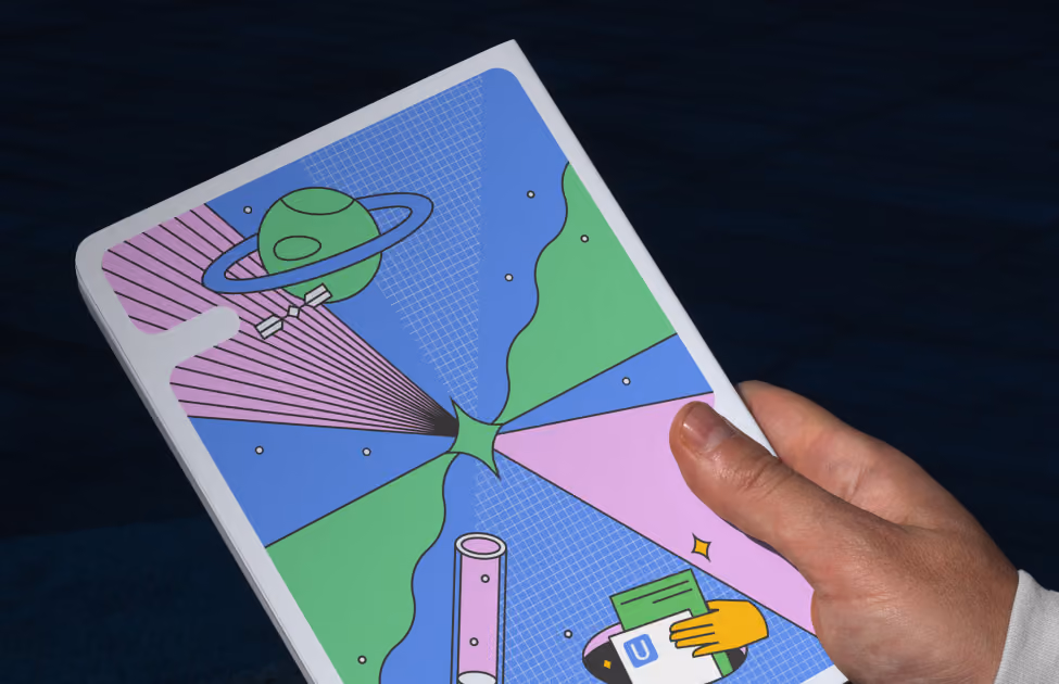 Hand holding a tablet with a colorful abstract design featuring planets, shapes, and a letter U.