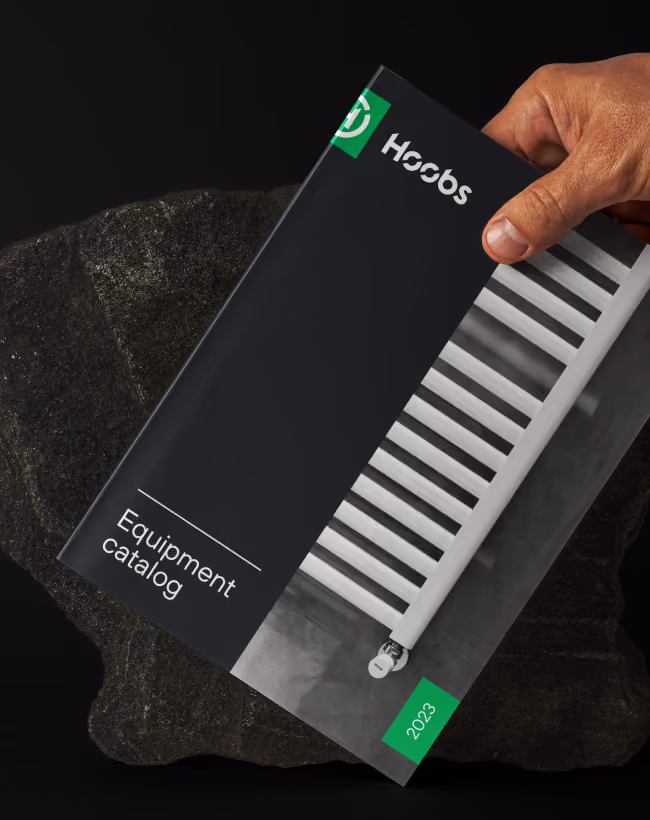 Hand holding a 2023 Hosbos Equipment catalog featuring a white radiator on the cover.