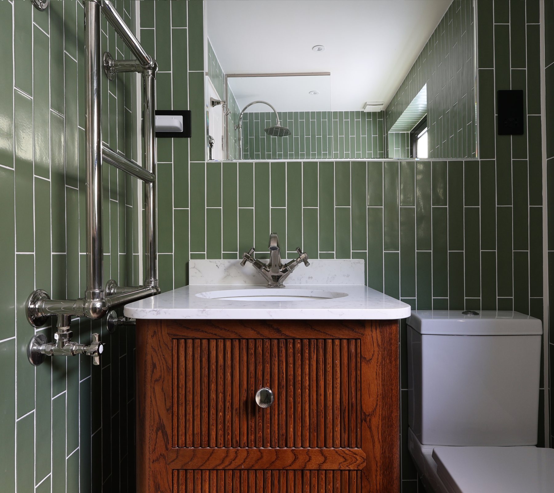 A family bathroom in a Battersea house finished in sage green metro tiles, with a walnut vanity, marble top, traditional brassware and a heated towel rail.