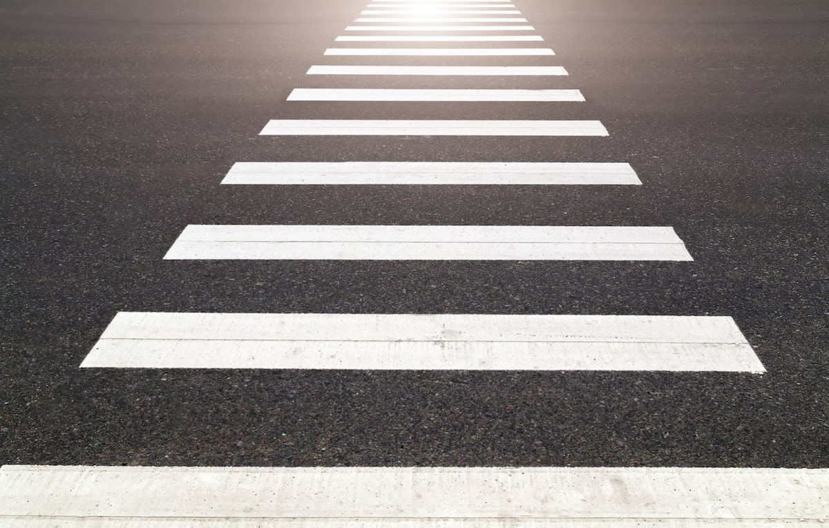Empty pedestrian crosswalk with white stripes on black asphalt road.
