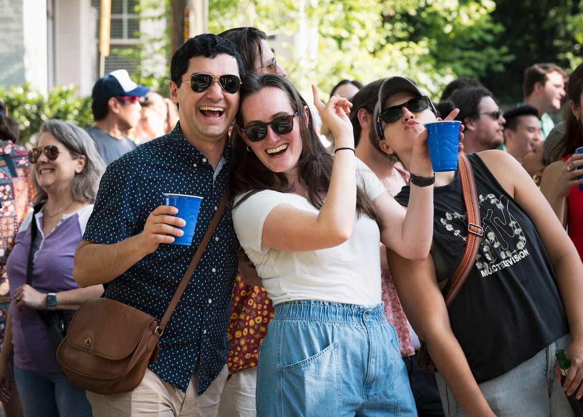 Friends wearing sunglasses smiling and holding blue cups at an outdoor gathering.