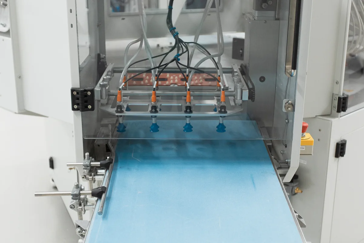 Unload section of a white machine with blue suction cups and a blue conveyor belt