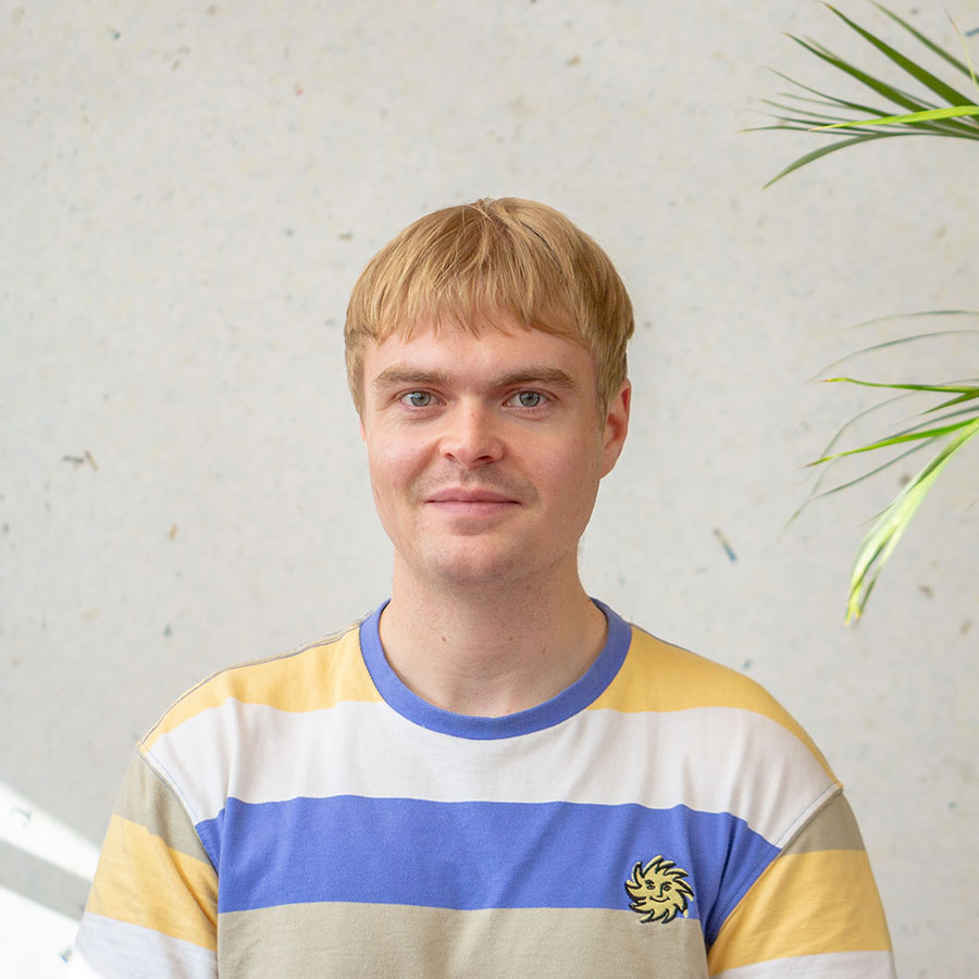 Dan smiling at the camera with blond hair and yellow and blue striped t-shirt