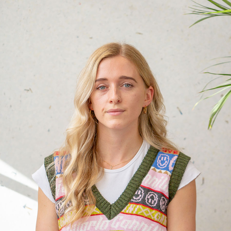 Lucy Williams looking at the camera, wearing a colourful knit vest over a white tee.