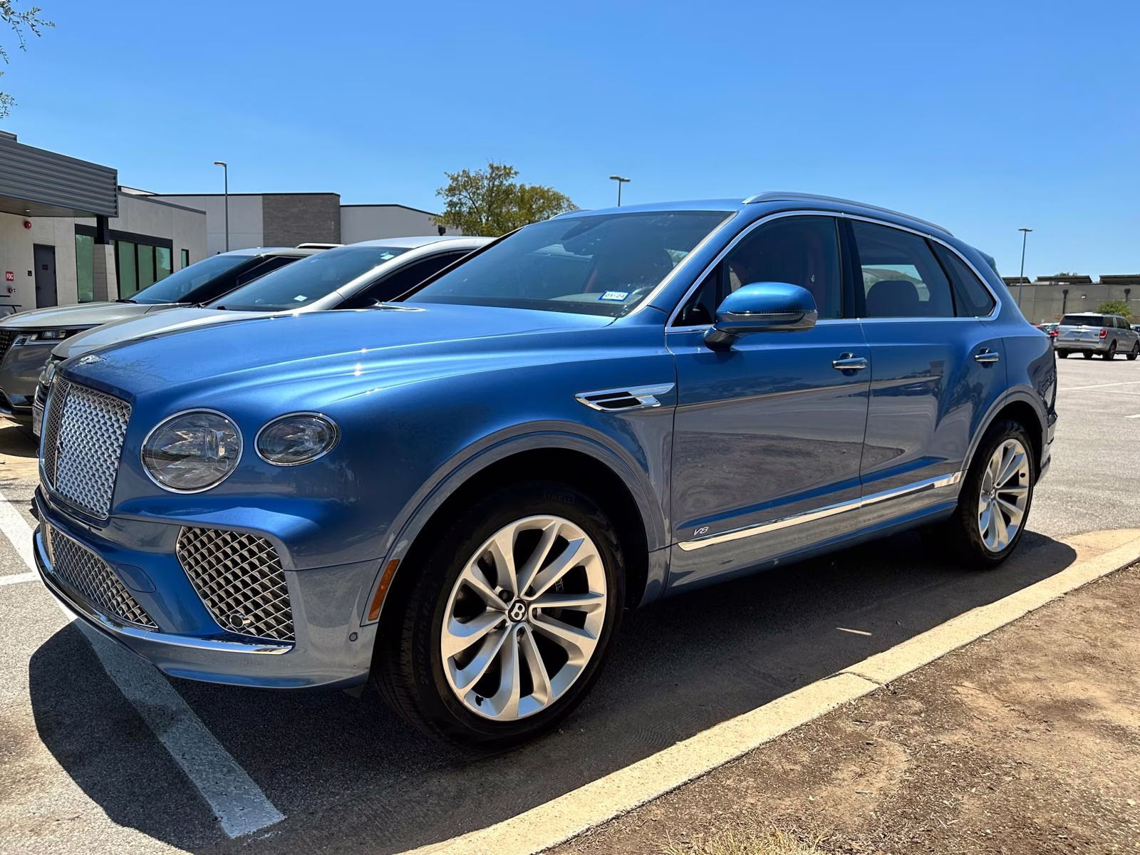 Blue Bentley Bentayga SUV parked in a lot under clear blue sky.