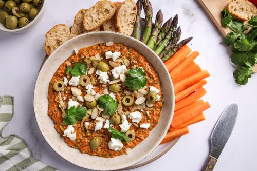Bowl of dip surrounded by bread and vegetable sticks