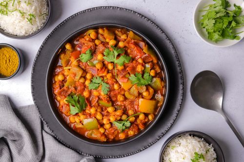 A vibrant bowl of Chickpea Jalfrezi Curry with golden chickpeas, red onion, and green capsicum in a rich tomato-based sauce, served alongside fluffy white rice and fresh coriander.
