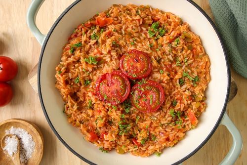 A hearty dish of Portuguese tomato rice (Arroz de Tomate) with vibrant red tomatoes, green capsicum, and fresh parsley.