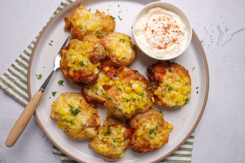 Close-up of crispy, golden smashed potatoes topped with melted cheese and sweetcorn, served with a dollop of sour cream.