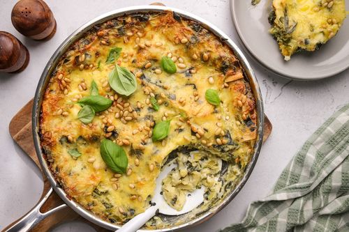 Golden, cheesy green lasagne bake in a pan, topped with pine nuts and bubbling melted cheese, loaded with Brussels sprouts, leek and silverbeet.