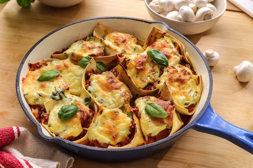 Close-up of a baked veggie lasagne pie with golden cheese topping and visible pumpkin, mushrooms, and greens in folded pasta cups.