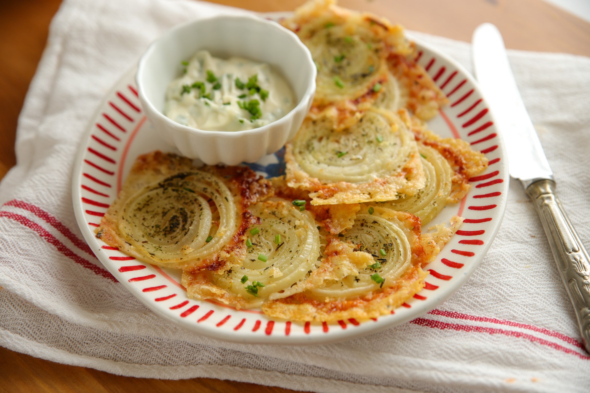 Golden parmesan crisps topped with roasted onion slices on a plate – the perfect cheesy side or snack.