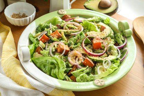 Colourful spring salad made with roasted kumara, avocado, shredded greens, and broccoli, topped with sesame seeds and tamari-ginger dressing.