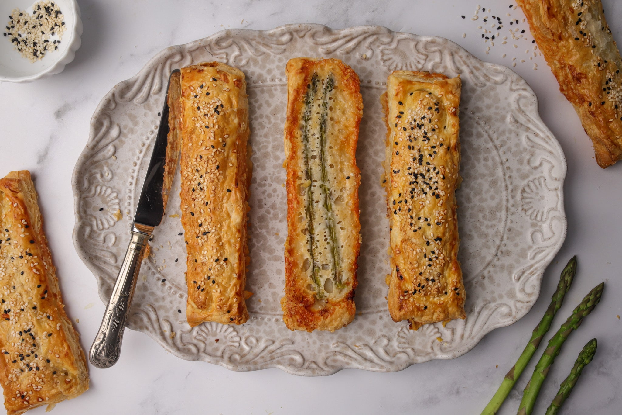 Golden puff pastry wrapped around roasted asparagus, topped with sesame seeds and melted Parmesan — fresh from the oven on baking paper.