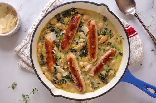 Hearty sausage, leek and butter bean stew in a white bowl, finished with wilted silverbeet and a sprinkle of parmesan.